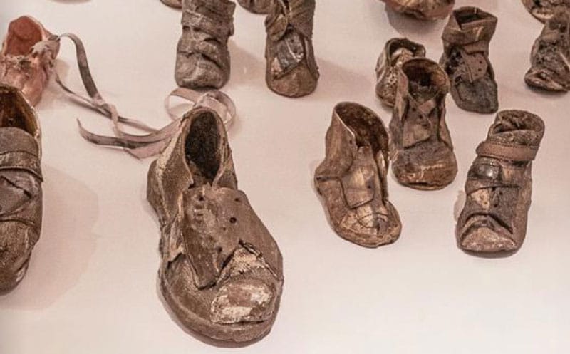 Worn, preserved shoes of various sizes are displayed on a light surface, symbolizing personal stories and history connected to a significant event or place.