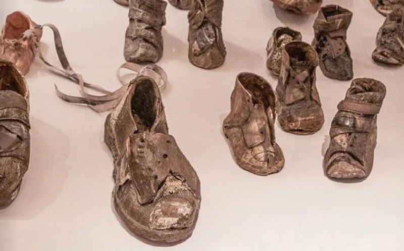 Worn, preserved shoes of various sizes are displayed on a light surface, symbolizing personal stories and history connected to a significant event or place.